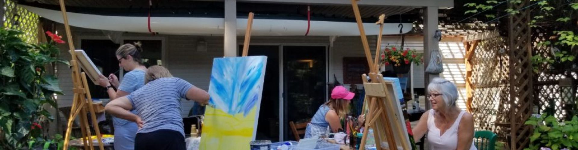 A group of people painting on canvasses outside of a house, they are at one of the classes of Linda Lovisa.