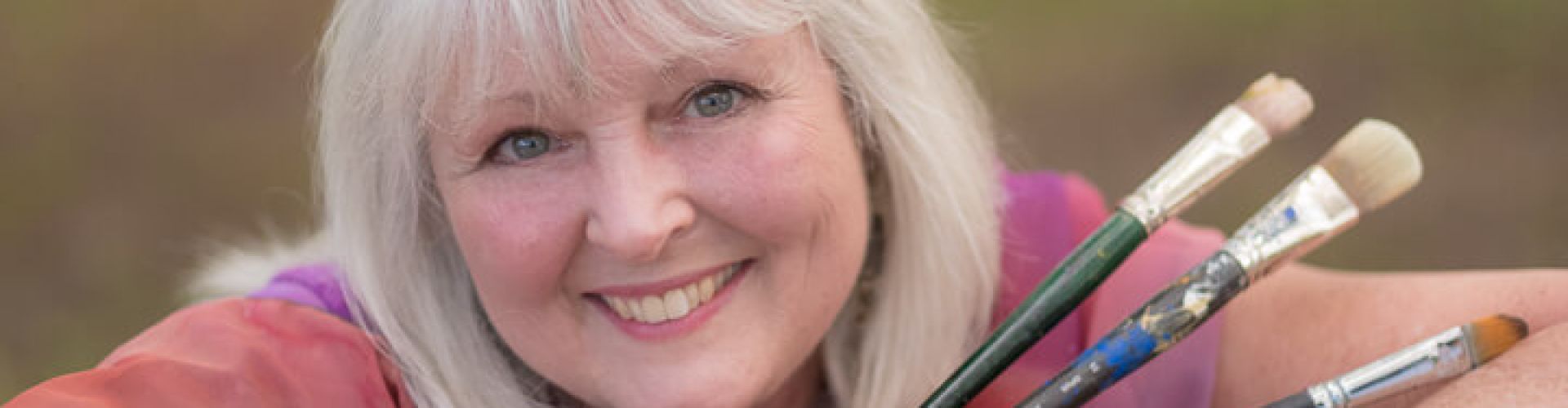 A close-up shot of Linda Lovisa while holding three paint brushes.