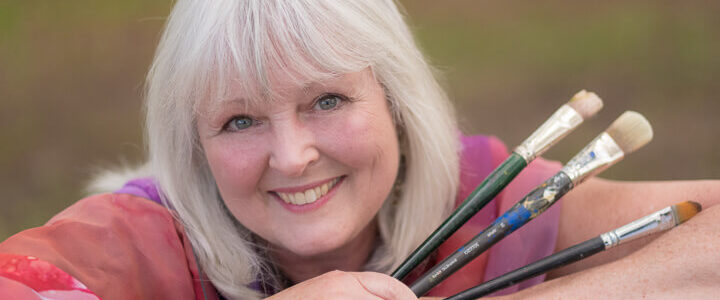 A close-up shot of Linda Lovisa while holding three paint brushes.