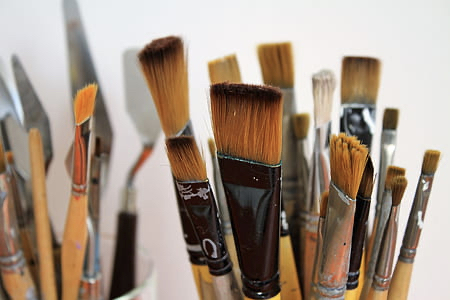 A close up shot of Canadian Artist Linda Lovisa's paint brushes, which are mostly flat and squared off style brushes on wooden handles, inside some brush holders in front of a white background.